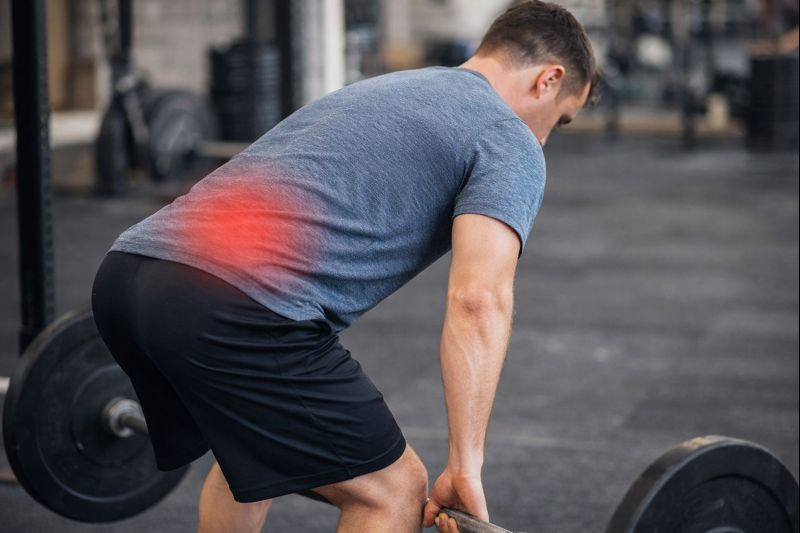 Adult lifter hip-hinging with a subtle red highlight over the low back to indicate lifting-related pain.