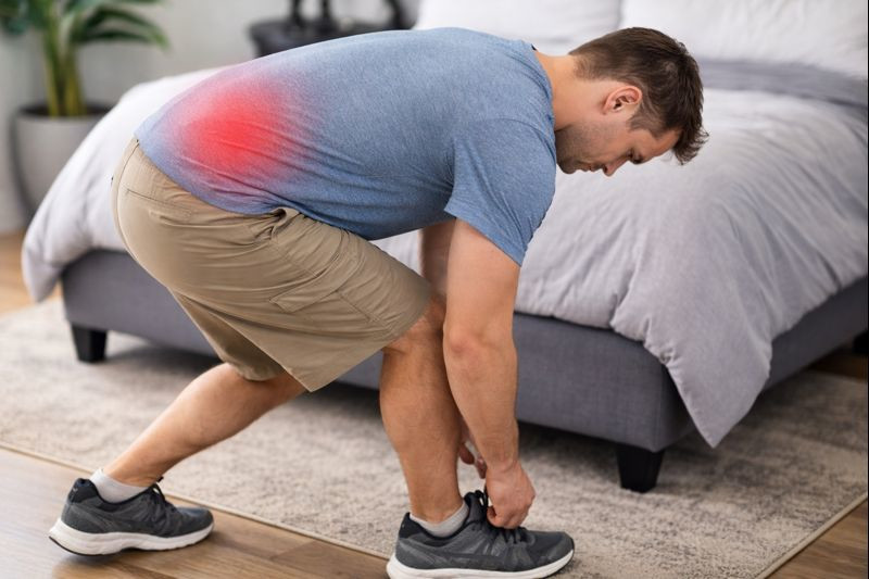 Adult bending over to tie shoes with a subtle red highlight over the low back indicating pain.
