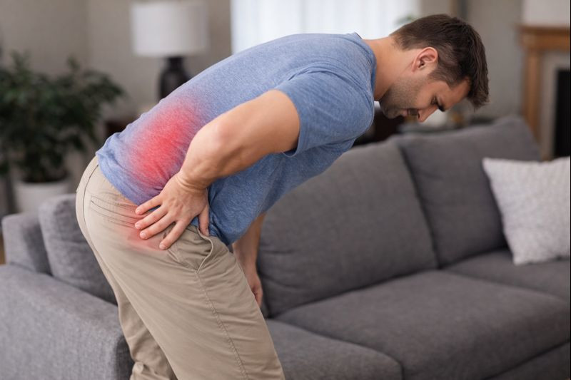 Adult standing up from a seated position with a subtle red highlight over the low back indicating pain.