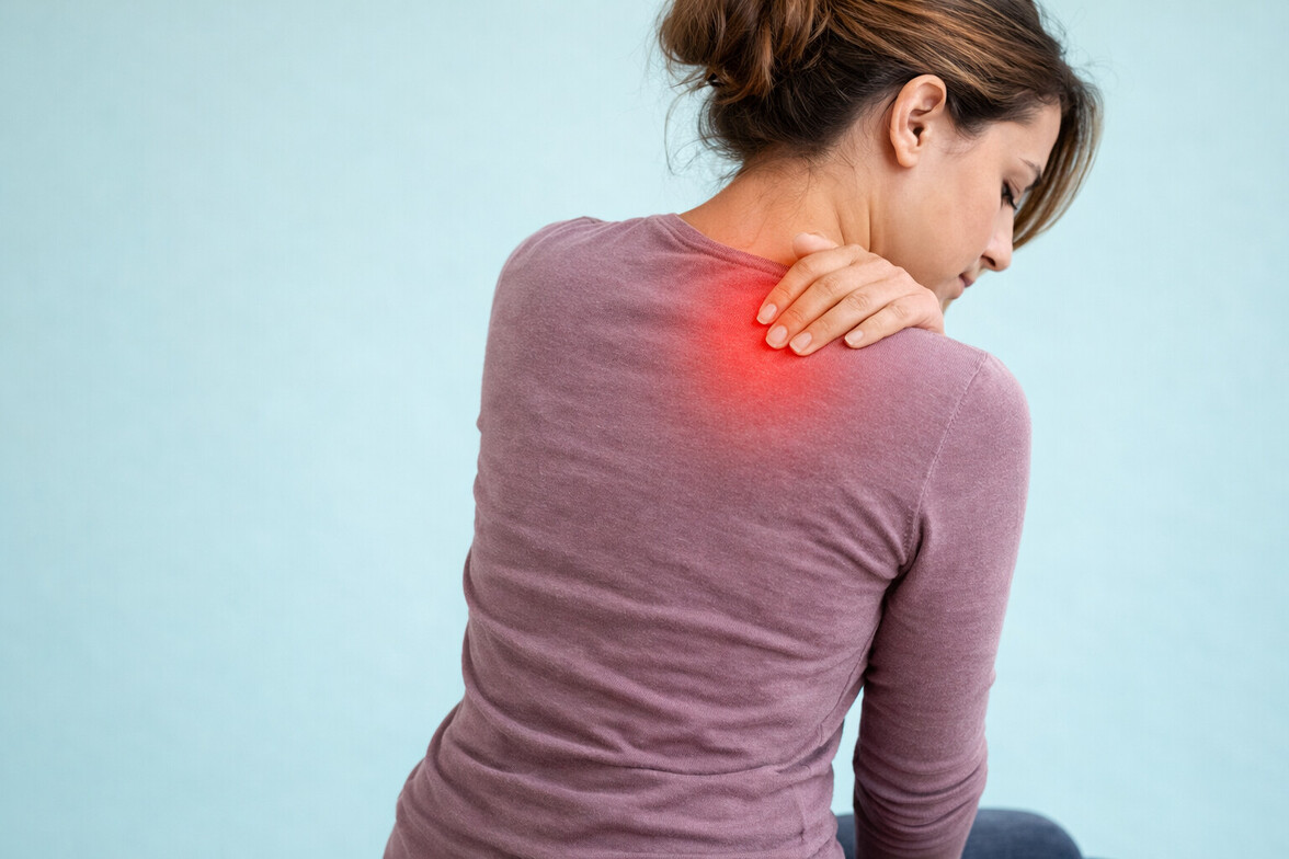 Rear view of person touching upper back with subtle red indicator showing chronic tightness in Olathe